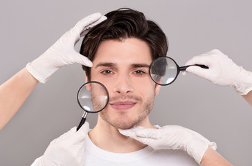 Face of young handsome man with beautician's hands and magnifiers