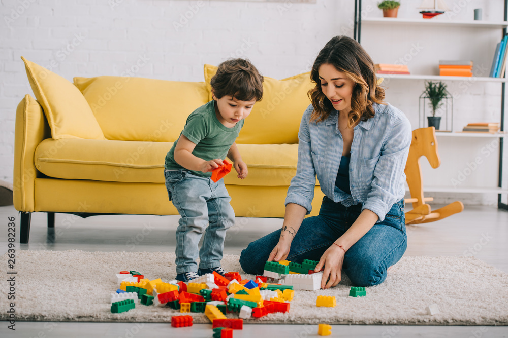 Wall mural Mother and son playing with Bricks on carpet in living room