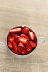 Cut strawberries in an artisan ceramic bowl, wooden background. Selective focus.
