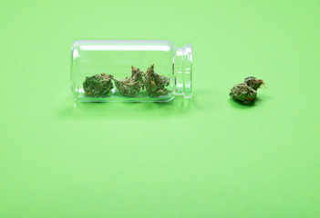 Dried medical cannabis buds in a glass bottle on green background. 