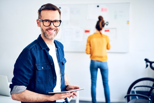 Portrait of smiling businessman in office with woman in background