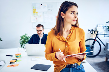 Businesswoman holding tablet in office with colleague in background