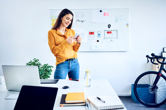 Smiling businesswoman holding smartphone at whiteboard in office