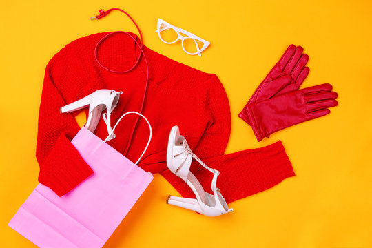 Top view of pink shopping bag with red swether, stylish shoes, red belt and gloves and white glasses