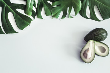 Avocado with tropical leaves on white background