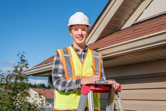 Home inspector standing on a ladder and providing an inspection to the roof of a house.