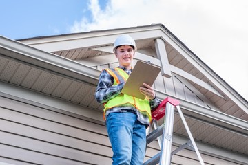 Home inspector standing on a ladder and providing an inspection to the roof of a house.