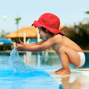 Little baby have a fun with a splash near swimming pool.