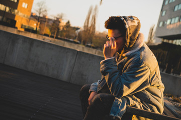 A young rapper in a city sitting at sunrise. - obrazy, fototapety, plakaty
