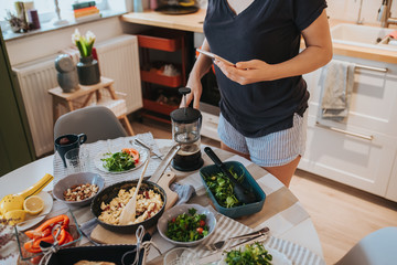 Breakfast table and woman holding smartphone in one hand navigating on social media and holding a big coffee filter glass mug with other hand, poring coffee.