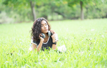 Beautiful Young Asian Woman lying on grass with Headphones and looking away happly. Enjoying Music