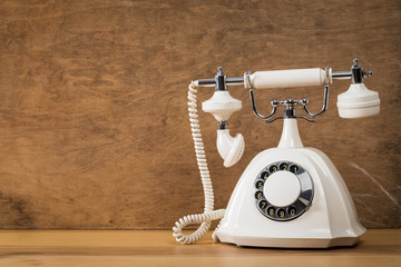  old white telephone on wooden table with color wall background