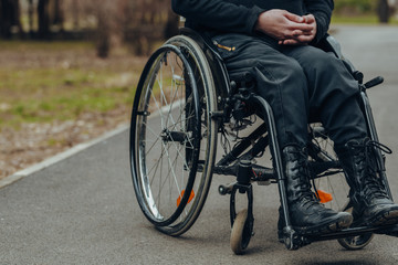 Obraz premium Close-up of male hand on wheel of wheelchair during walk in park