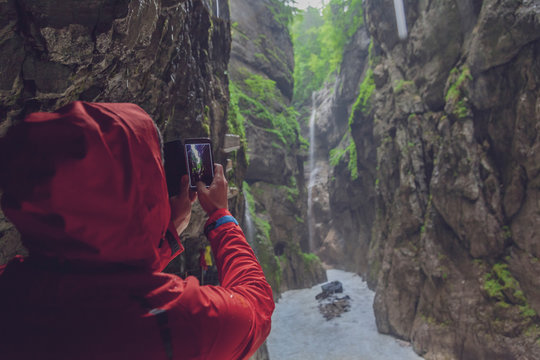 Germany, Bavaria, Partnach Gorge near Garmisch-Partenkirchen, man with red rain jacket taking a photo with smartphone
