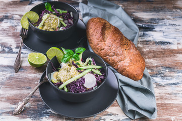 Italian ciabatta and fresh vegetable salad in a dark bowl. Salad with radish, red cabbage, cucumber, pesto and sesame seeds.