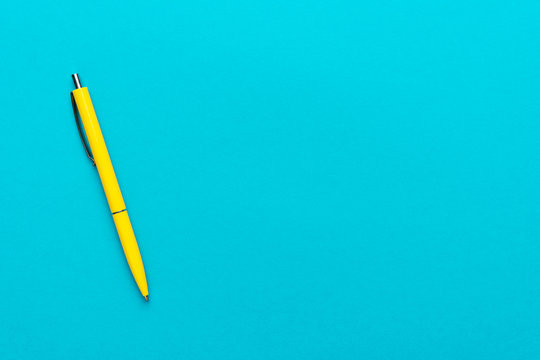 photo of yellow ballpoint pen over turquoise blue background with copy space