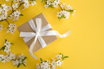 Gift with white bow and flowering tree branches on the yellow background.Top view.Copy space.