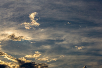 Floating clouds illuminated by the sunset light, against an almost clear sky, above the Andean mountains of central Colombia.