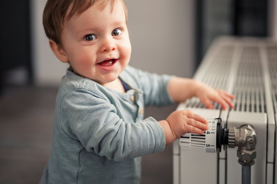 Portrait of smiling baby boy playing with thermostat of heater