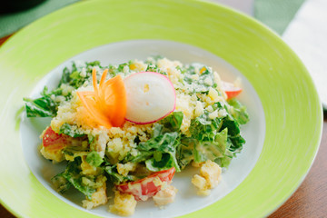 Salad with radish, carrot, lettuce and cheese in a green plate.