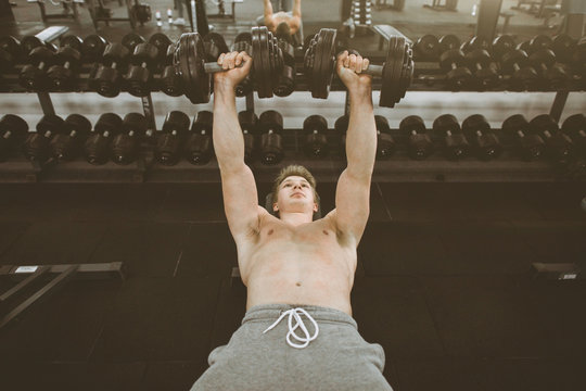 Handsome young phisique fitness man works out in gym lifting dumbbells. Man bodybuilder exercising at gym holding dumbbells