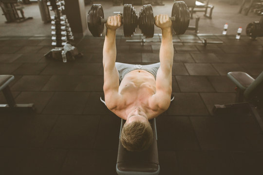 Handsome young phisique fitness man works out in gym lifting dumbbells. Man bodybuilder exercising at gym holding dumbbells