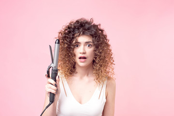 Beautiful woman with a surprised facial expression with amazing curls in a white shirt holds in her hand accessories for hair styling