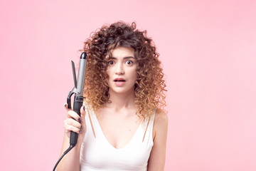 Beautiful woman with a surprised facial expression with amazing curls in a white shirt holds in her hand accessories for hair styling