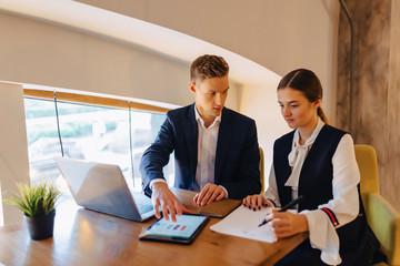 young businessmen boy and girl work with a laptop, a tablet and notes in the cafe
