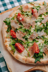 Neapolitan pizza with salami, arugula, tomatoes sprinkled with cheese on a wooden board on a tablecloth in a cell with a place for text