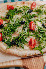 Neapolitan pizza with tuna, cheese, arugula, basil, tomatoes, olives, sprinkled with cheese on a wooden table on a tablecloth in a cell with a place for the text.