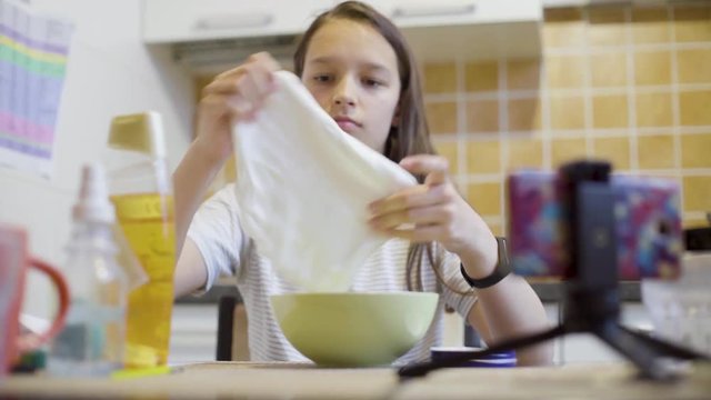 school girl stretching and squeezing homemade fluffy slime on the kitchen