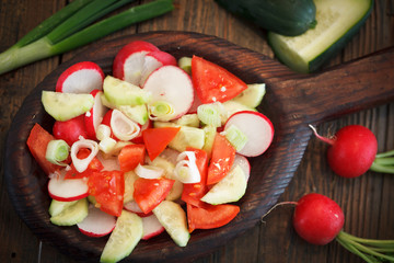 Top view of Healthy vegetable salad of fresh tomato, cucumber, onion and red radish on rustic, wooden plate. Diet menu.