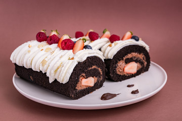 Chocolate roll cake with berries and fresh cream on brown background.