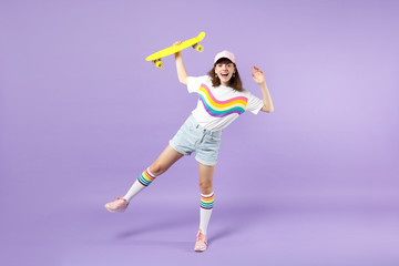 Portrait of cheerful teen girl in vivid clothes having fun holding yellow skateboard isolated on violet pastel wall background in studio. People sincere emotions lifestyle concept. Mock up copy space.