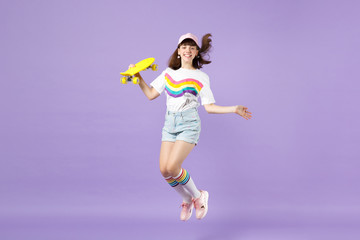 Fototapeta na wymiar Portrait of cheerful teen girl in vivid clothes holding yellow skateboard, having fun jumping isolated on violet pastel wall background. People sincere emotions, lifestyle concept. Mock up copy space.