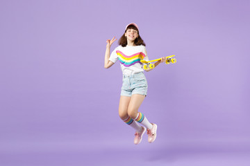 Fototapeta na wymiar Pretty teen girl in vivid clothes holding yellow skateboard showing victory sign having fun jumping isolated on violet pastel background. People sincere emotions lifestyle concept. Mock up copy space.