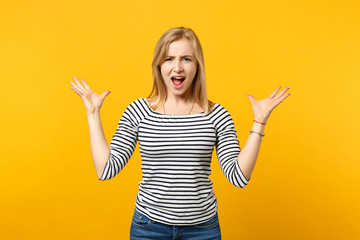 Portrait of irritated young woman in striped clothes screaming, swearing spreading hands isolated on yellow orange background in studio. People sincere emotions, lifestyle concept. Mock up copy space.