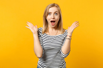 Excited young woman in striped clothes keeping mouth wide open, spreading hands isolated on yellow orange wall background in studio. People sincere emotions, lifestyle concept. Mock up copy space.