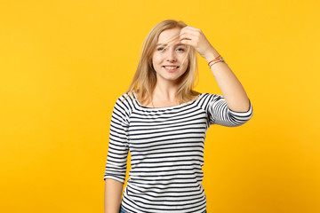 Portrait of beautiful joyful young woman in striped clothes holding hair looking camera isolated on yellow orange background in studio. People sincere emotions, lifestyle concept. Mock up copy space.