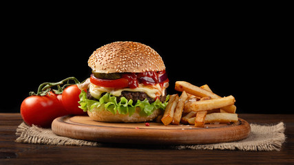 Homemade hamburger close-up with beef, tomato, lettuce, cheese and french fries on cutting board
