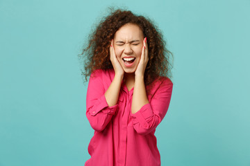 Screaming african girl in pink casual clothes keeping eyes closed, covering ears with hands...