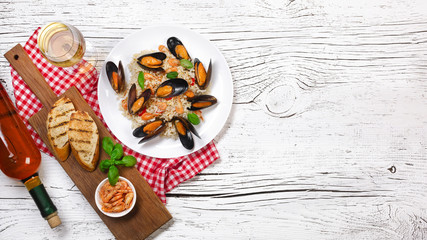 Fried rice with seafood mussels, shrimps and basil in a plate with wine bottle, wineglass, towel and toasted baguette on white cracked wooden table