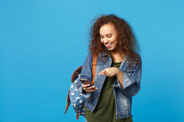 Young african american girl teen student in denim clothes, backpack hold phone isolated on blue wall background studio portrait. Education in high school university college concept. Mock up copy space