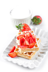 Belgium waffers with sugar powder and strawberries on ceramic plate on white table.