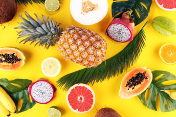 Exotic fruits and tropical palm leaves on pastel yellow background - papaya, mango, pineapple, banana, carambola, dragon fruit