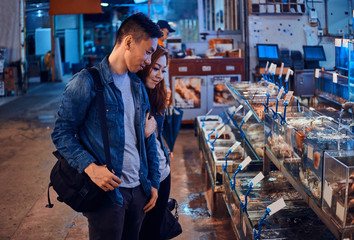 Fototapeta premium Romantic asian couple looking for something special at seafood chainese market. They are curious and joyful.
