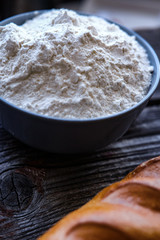 Closeup photo of bowl of white flour and bread on black wooden table.