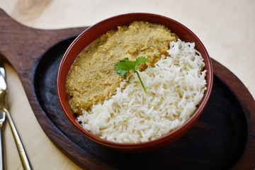 There are indian traditional curry dish with rice and coriander leaf on wooden tray.