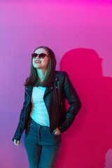 Fashioned girl in leather jacket in dark glasses in pink anf blue  neon lights background. 